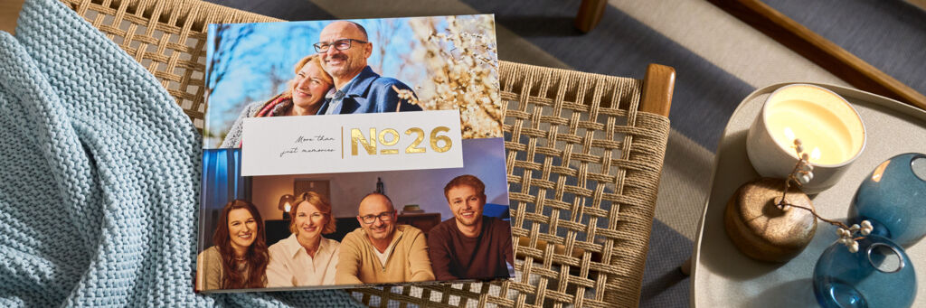 CEWE FOTOBUCH „N°26“ mit Fotos eines Paares und einer Familie von vier Personen auf einem geflochtenen Stuhl mit blauer Decke.