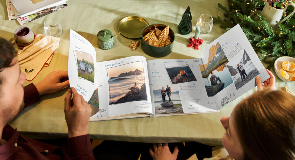 Ein Pärchen sieht sich gemeinsam die aufgeklappten Seiten einer Panoramaseite in einem CEWE FOTOBUCH an.