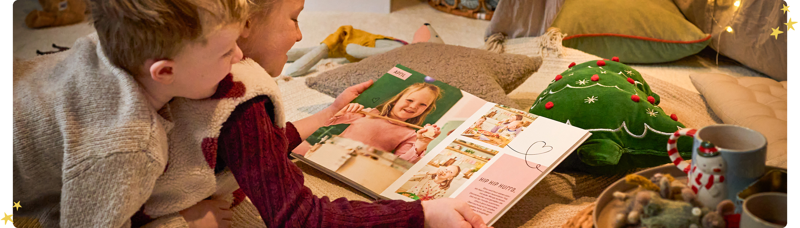 Zwei Kinder betrachten gemeinsam ein CEWE FOTOBUCH in gemütlicher Weihnachtsstimmung