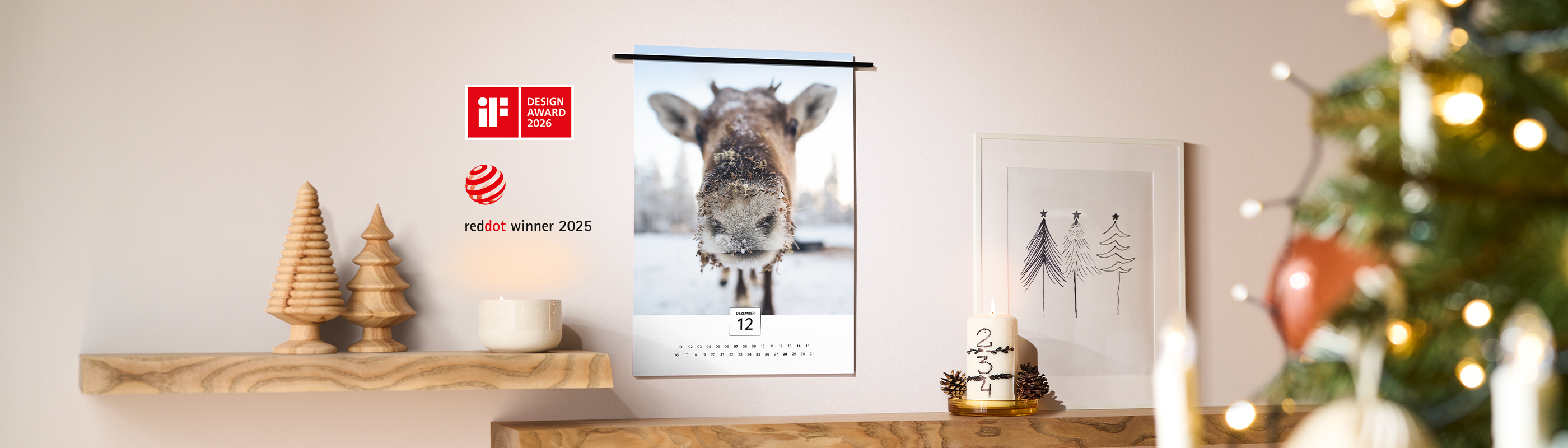 CEWE Fineline Wandkalender mit Rentierfoto im Winter hängt an Wand, umgeben von Weihnachtsdeko, iF Design Award 2026 und Red Dot Winner 2025